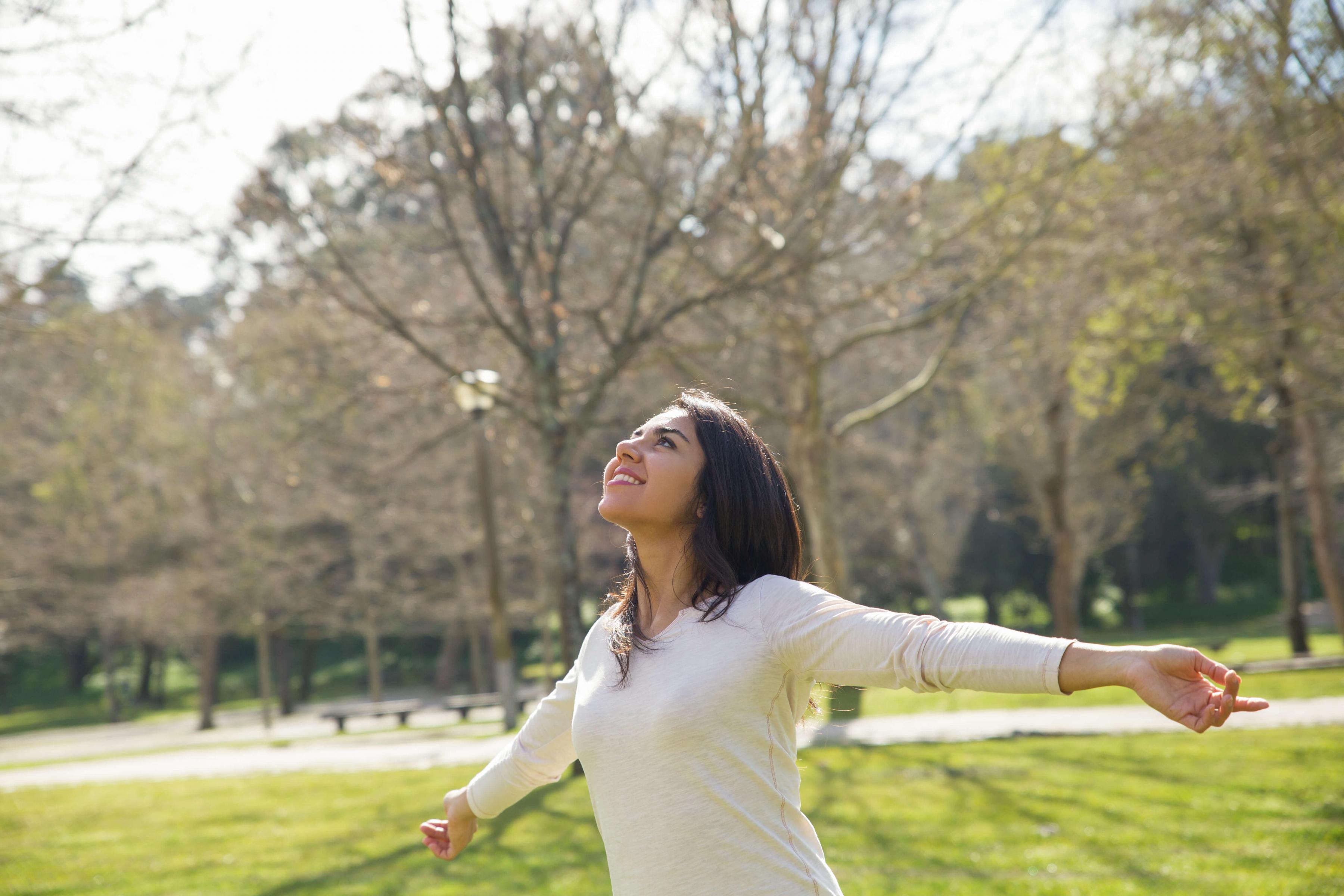 Image of woman in park with arms open looking at sky